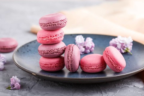 Purple and pink macaron or macaroon cakes with lilac flowers on blue ceramic plate on a gray