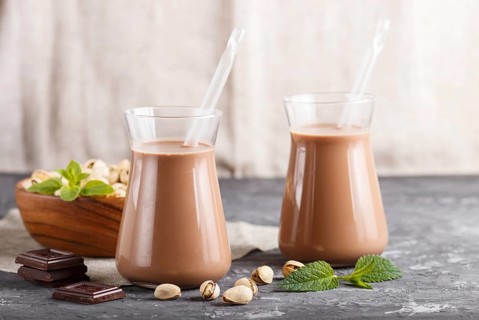 Organic non dairy pistache chocolate milk in glass and wooden plate with pistache nuts on a gray