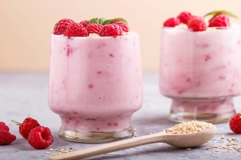Yoghurt with raspberry and sesame in a glass and wooden spoon on gray and orange background. side