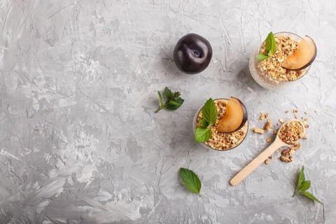 Yoghurt with plum, chia seeds and granola in a glass and wooden spoon on gray concrete background.