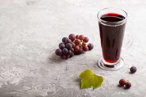 Glass of red grape juice on a gray concrete background. Morninig, spring, healthy drink concept.