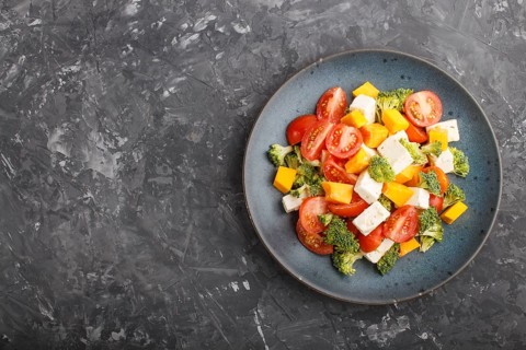 Vegetarian salad with broccoli, tomatoes, feta cheese, and pumpkin on a blue ceramic plate on a