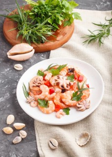 Boiled shrimps or prawns and small octopuses with herbs on white ceramic plate on a black concrete