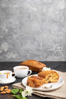 Homemade cake with raisins, almonds, soft caramel and a cup of coffee on a black concrete
