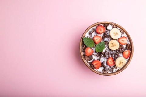 Chocolate cornflakes with milk and strawberry in wooden bowl on pink pastel background. Top view,