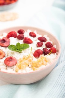 Rice flakes porridge with milk and strawberry in ceramic bowl on white concrete background and blue