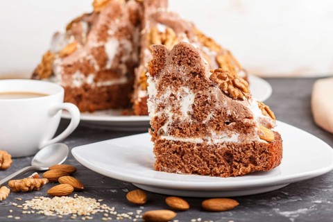 Homemade cake with milk cream, cocoa, almond, hazelnut on a black concrete background and a cup of
