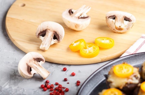 Sliced raw champignons with kumquats on a gray concrete background. ceramic plate, side view, close