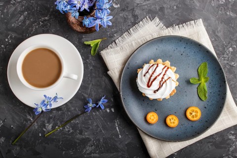 Cake with whipped egg cream on a blue ceramic plate with kumquat slices and mint leaves on a black