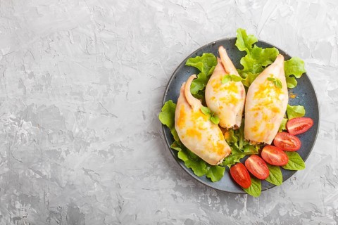 Stuffed baked squid with greens on a blue ceramic plate on a gray concrete background, top view,
