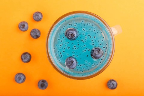 Glass of blueberry blue colored drink with basil seeds on orange background. Morninig, spring,