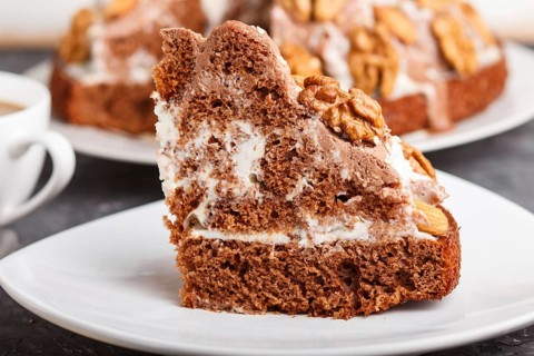 Homemade cake with milk cream, cocoa, almond, hazelnut on a black concrete background and a cup of