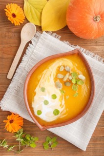 Traditional pumpkin cream soup with seeds in clay bowl on a brown wooden background with linen