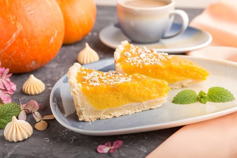 Two pieces of traditional american pumpkin pie with cup of coffee on a black concrete background