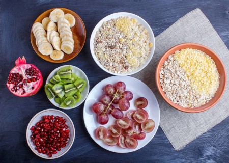 A set of plates with muesli, grapes, kiwi, pomegranate, banana on a black wooden background. top