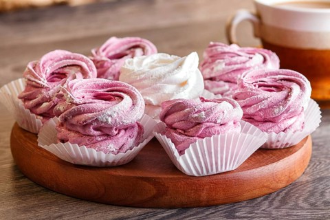 Pink and white marshmallows (zephyr) on a round wooden board with cup of coffee on a gray wooden