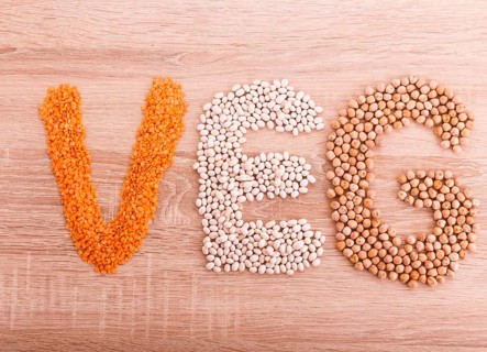 Word Vegan made of lentils, buckwheat, beans, rice and chickpeas on a wooden background