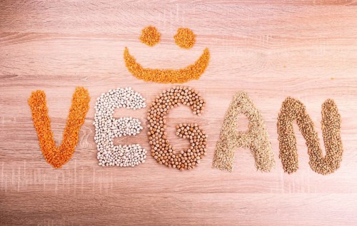 Word Vegan with a smile made of lentils, buckwheat, beans, rice and chickpeas on a wooden
