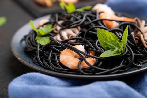 Black cuttlefish ink pasta with shrimps or prawns and small octopuses on black concrete background