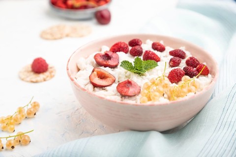 Rice flakes porridge with milk and strawberry in ceramic bowl on white concrete background and blue