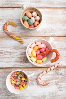 Heap of multicolored caramel candies in cups on white wooden background. close up, top view, flat