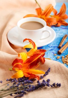 Orange day-lily and lavender flowers and a cup of coffee on a blue concrete background, with orange