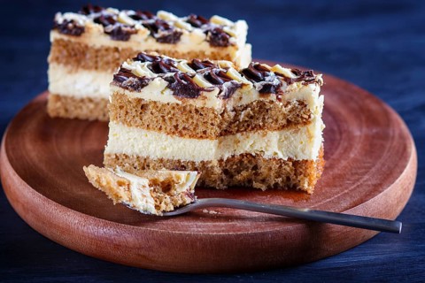 A piece of cake with milk and butter cream cutted with spoon on a wooden kitchen board, close up,