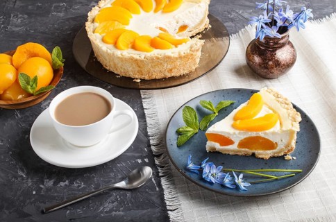 A piece of peach cheesecake on a blue ceramic plate with blue flowers and a cup of coffee on a