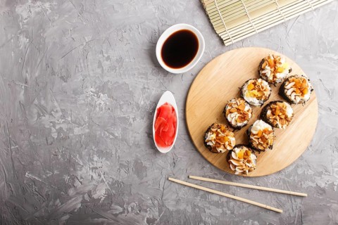 Japanese maki sushi rolls with cream cheese, chopsticks, soy sauce and marinated ginger on wooden