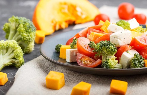 Vegetarian salad with broccoli, tomatoes, feta cheese, and pumpkin on a blue ceramic plate on a