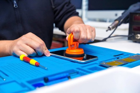 Unrecognizable male technician opening the screen of a mobile using suction cup in a small workshop