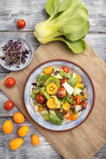 Vegetarian salad of pac choi cabbage, kiwi, tomatoes, kumquat, microgreen sprouts on gray wooden