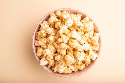 Popcorn with caramel in ceramic bowl on pastel orange background. Top view, flat lay, close up