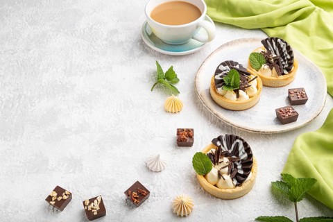 Sweet tartlets with chocolate and cheese cream with cup of coffee on a gray concrete background and
