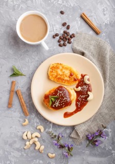 Cheese pancakes with caramel sauce on a beige ceramic plate and a cup of coffee on a gray concrete
