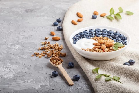 Yoghurt with blueberry, granola and almond in white plate with wooden spoon on gray concrete