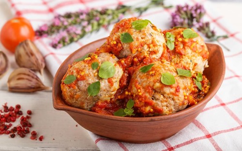 Pork meatballs with tomato sauce, oregano leaves, spices and herbs in clay bowl on a white wooden