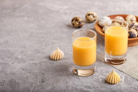Sweet egg liqueur in glass with quail eggs and meringues on a gray concrete background. Side view,