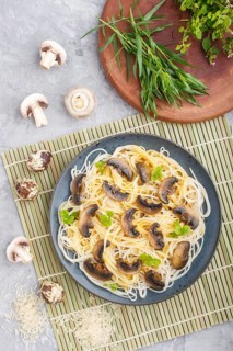 Rice noodles with champignons mushrooms, egg sauce and oregano on blue ceramic plate on a gray