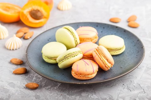Orange and green macarons or macaroons cakes on blue ceramic plate on a gray concrete background.