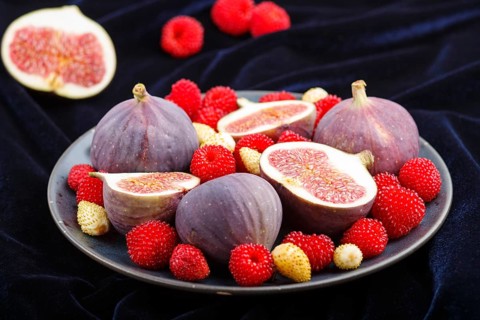 Fresh figs, strawberries and raspberries on blue ceramic plate on black concrete background and