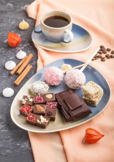 A pieces of homemade chocolate with coconut candies and a cup of coffee on a black concrete