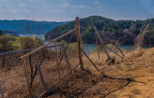 Broken metal gate and post sitting in field with lake and mountains in background on spring