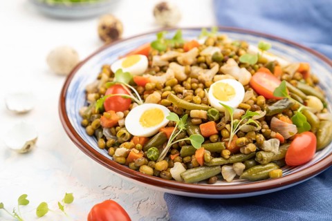 Mung bean porridge with quail eggs, tomatoes and microgreen sprouts on a white concrete background
