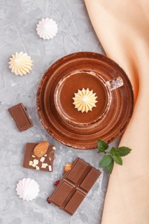 Cup of hot chocolate and pieces of milk chocolate with almonds on a gray concrete background with
