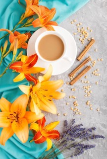 Orange day-lily and lavender flowers and a cup of coffee on a gray concrete background, with blue