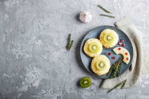 Pieces of baked pork with pineapple, cheese and kiwi on gray background, top view, copy space