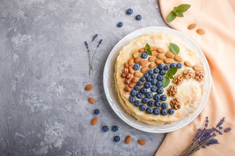 Homemade layered Napoleon cake with milk cream. Decorated with blueberry, almonds, walnuts,