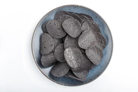 Black potato chips with charcoal on a blue ceramic plate isolated on white background. Top view,