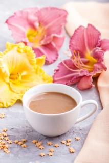 Yellow anf purple day-lilies cup of coffee on a gray concrete background, with orange textile.